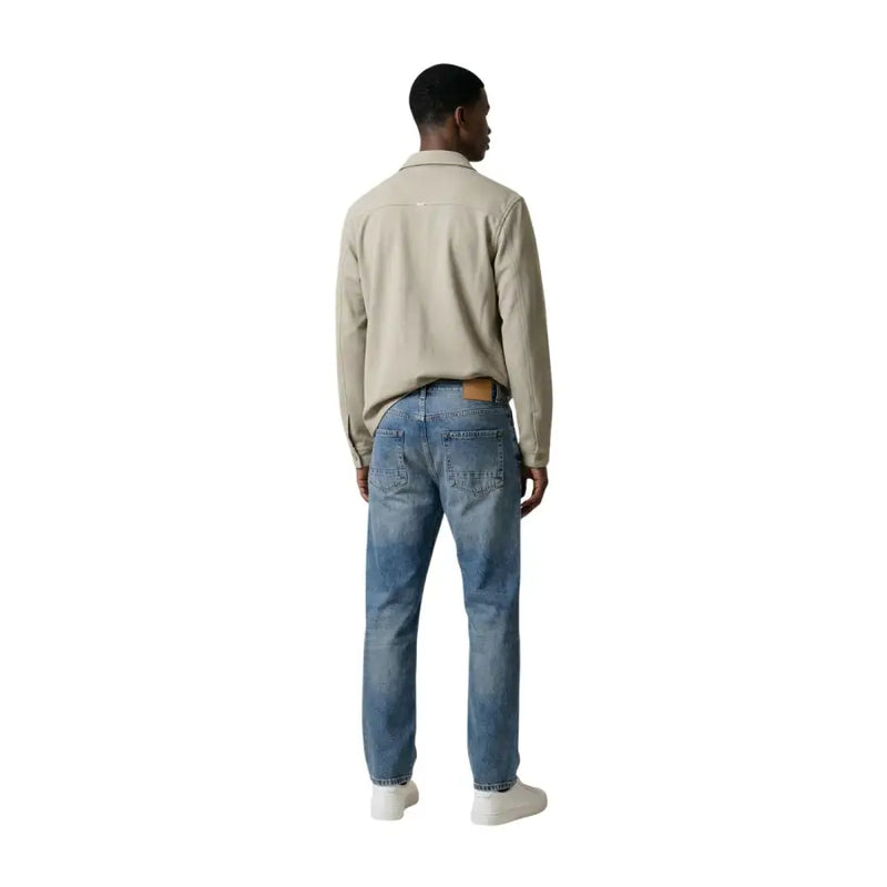 Antony Morato Ein beigefarbener Baumwollblazer für Herren wird über einem beigefarbenen Baumwollhemd mit Kragen und langen Ärmeln getragen, dazu eine blaue Jeans.