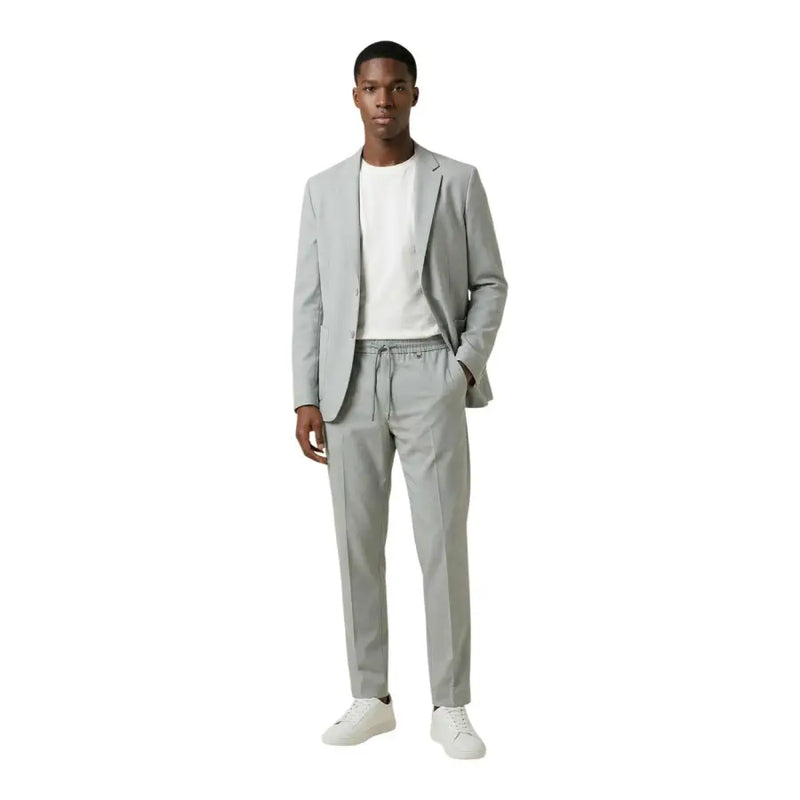 Antony Morato Grauer Herrenblazer aus Polyester mit V-Ausschnitt und Revers, kombiniert mit einer eleganten, hellgrauen Stoffhose mit Kordelzug und weißen Sneakers.
