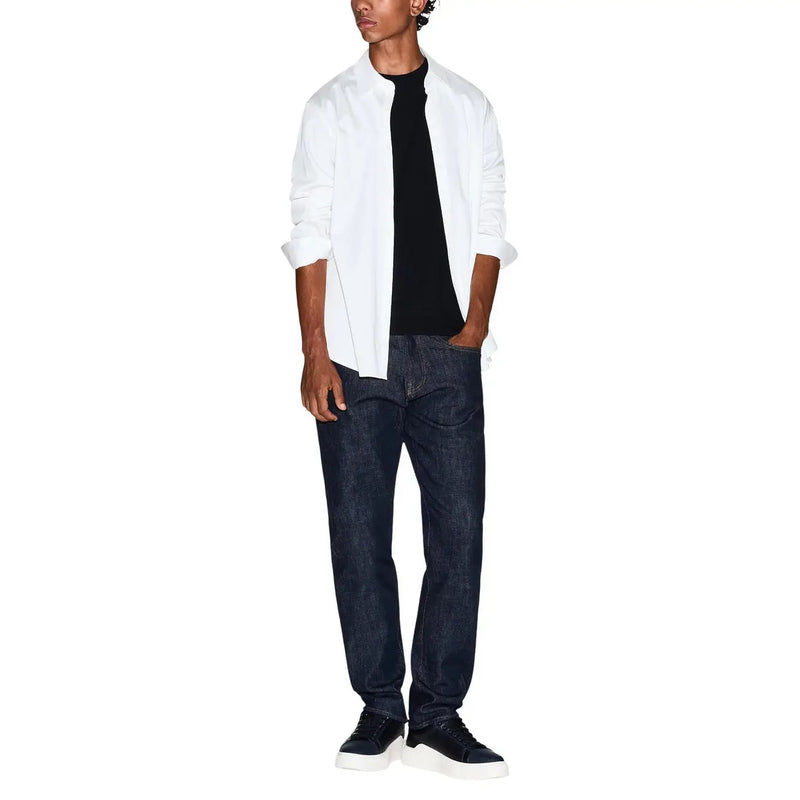 Ein Mann, der einen Armani Exchange Schwarzes Baumwoll-T-Shirt für Herren kombiniert mit einem weißen Hemd, dunkelblauen Jeans und schwarzen Sneakers