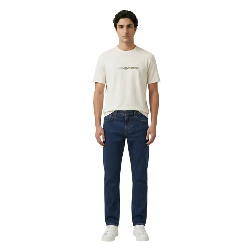 Ein Mann, der einen cremefarbenen Armani Exchange Männer t-shirt mit dezenter goldener Schrift und dunkelblauen Jeans