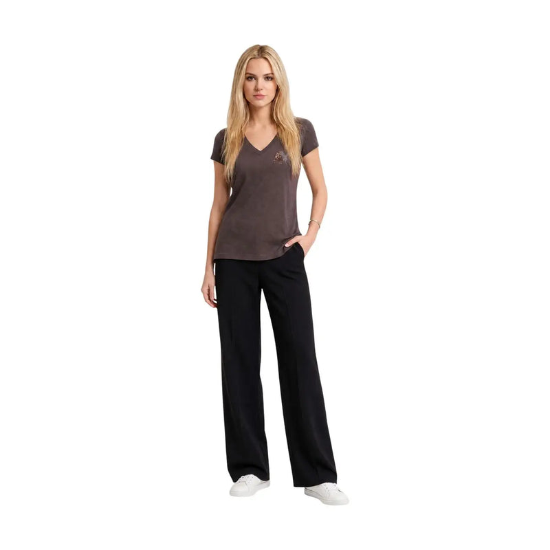 Eine Frau, die ein Armani Exchange Braunes Damen-T-Shirt aus Baumwolle mit V-Ausschnitt und Pailletten, kombiniert mit schwarzer Hose und weißen Sneakers