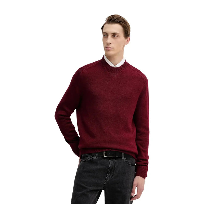Armani Exchange Herrenpullover aus Wolle in Burgunderrot mit geripptem Kragen und Bündchen, getragen über einem weißen Hemd mit Kragen, das vom Model getragen wird.