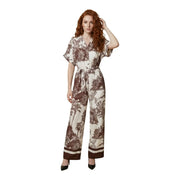 Eine Frau trägt einen beigefarbenen Artigli-Jumpsuit aus Viskose mit V-Ausschnitt, braunem Pflanzenmuster und passendem Taillengürtel.
