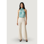 Eine Frau trägt eine weiße, weite Hose von Artigli mit Reißverschlusstaschen vorne, kombiniert mit einem türkisfarbenen Neckholder-Top im Batik-Look. top