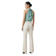 Eine Frau trägt eine weiße Artigli-Damenhose mit Reißverschlusstaschen vorne in Creme und ein türkisfarbenes Seiden-Neckholder-Top. top mit einer Schleife am Rücken