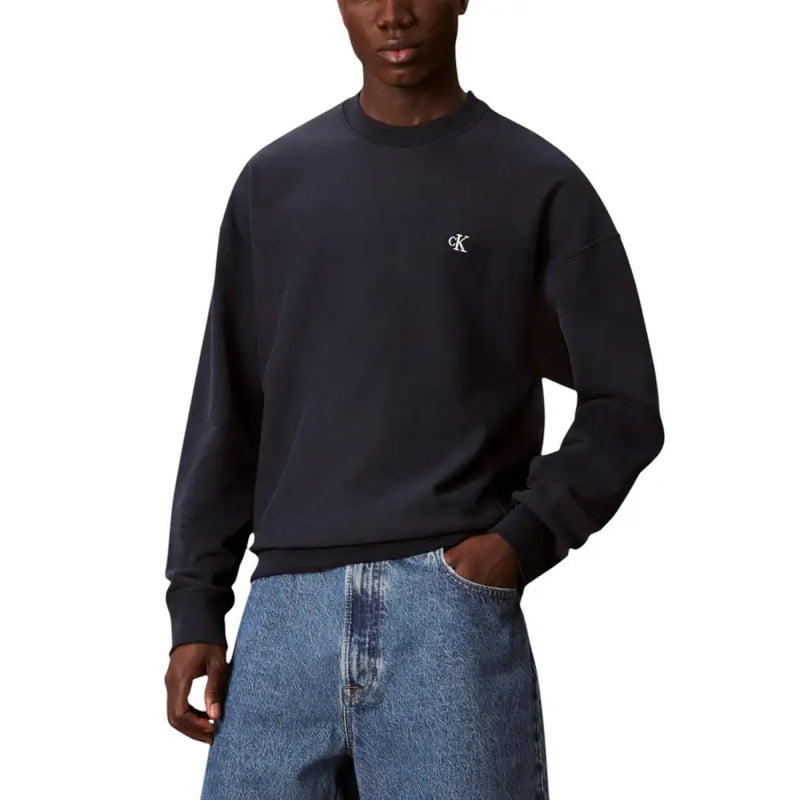 Beigefarbenes Sweatshirt mit Rundhalsausschnitt und dunkelblauem Calvin Klein-Sweatshirt mit kleinem, weißem, gesticktem Logo auf der Brust.