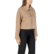 Woman in tan cropped utility jacket with zipper and chest pockets, wearing black pants