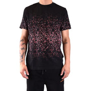 Schwarzes Kurzarm-T-Shirt mit rosa und weißen Glitzerpunkten, die von der Brust bis zum Saum in einem Spritzmuster auslaufen.