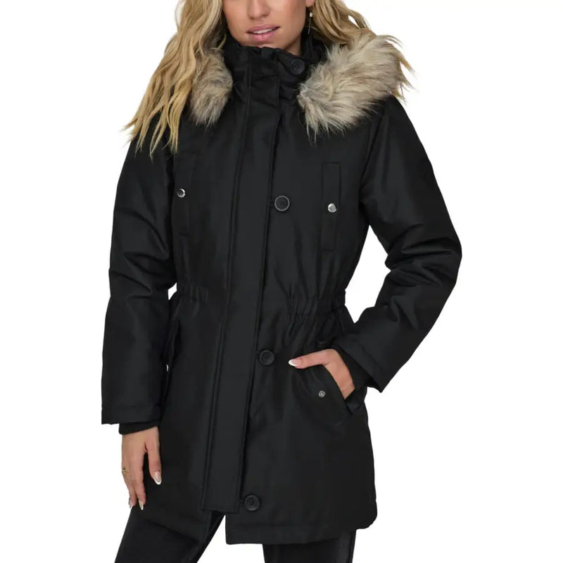 Black women’s jacket with hood and front pockets featuring a black winter parka style with tan faux fur-lined hood and silver buttons