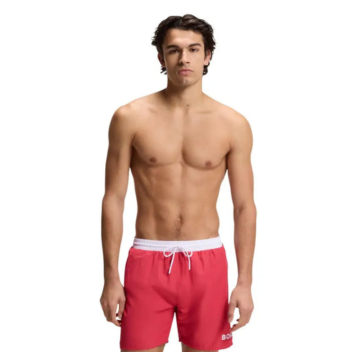 Red swim trunks with white elastic waistband and boss logo on lower right leg made of polyester with pockets
