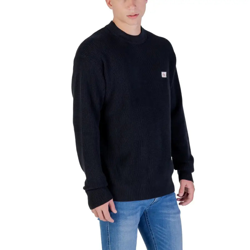 Black crewneck sweater with small white logo on chest, likely made of cotton or polyester blend.