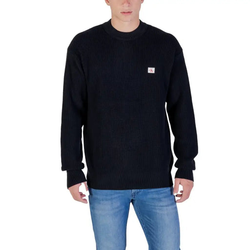 Black ribbed sweater with small logo on chest, likely made of cotton or wool.