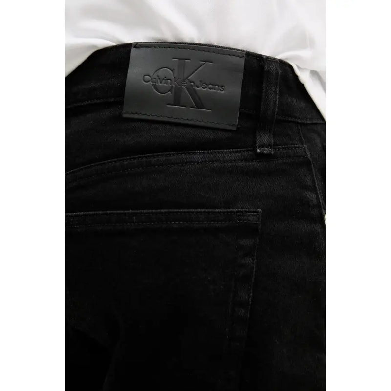 Black calvin klein jeans label with embossed ck logo on dark denim fabric of black cotton stretch shorts for men back side