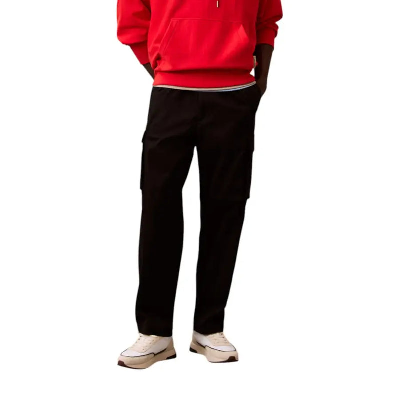 Men’s red hooded sweatshirt, black cargo pants, and white sneakers from Calvin Klein Jeans