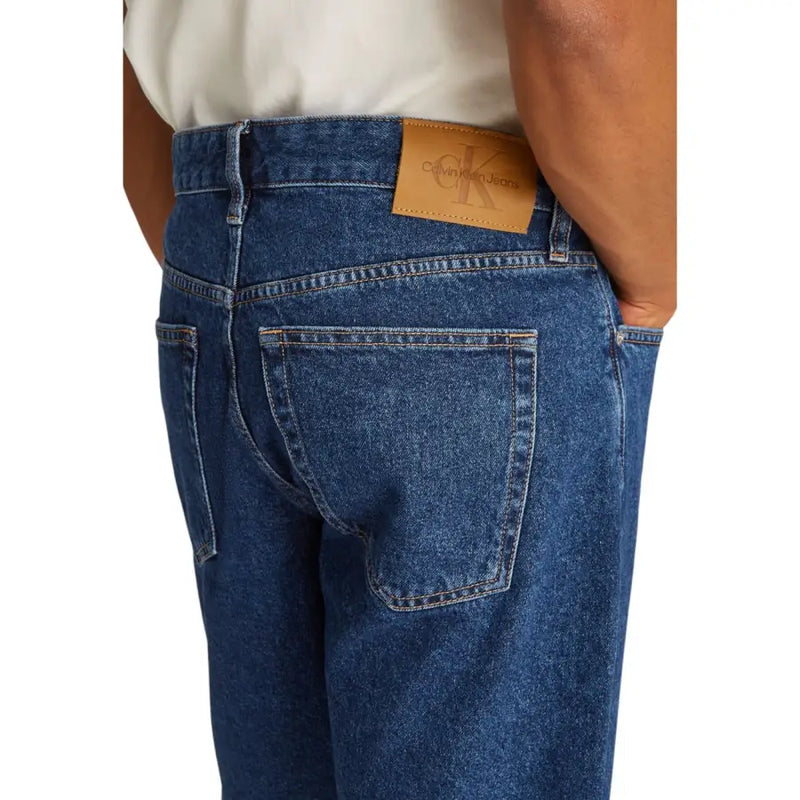 Blue denim jeans with tan leather patch featuring calvin klein jeans logo on light blue cotton shorts for men back view