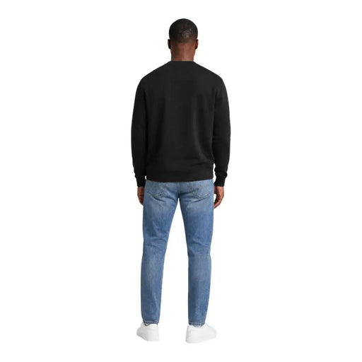 Black cotton crewneck sweatshirt with long sleeves paired with light-wash blue jeans by Calvin Klein Jeans men