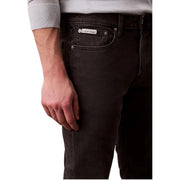 Image of the back side of dark wash Calvin Klein black cotton stretch men’s jeans with a brand label on the pocket