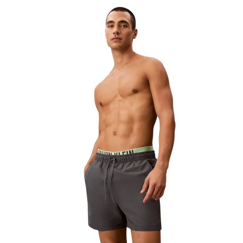 Calvin Klein Jeans Herren-Badeshorts aus grauem Polyester, Größe M, mit dunkelgrauem Rumpf und hellgrünem Logo am Bund.