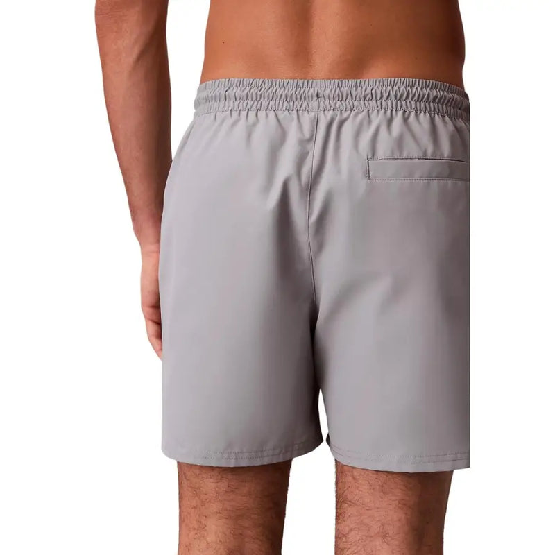 Calvin Klein Herren-Badeshorts aus grauem Polyester, Größe M, mit elastischem Bund und einer einzelnen Tasche, die Rückseite zeigt.