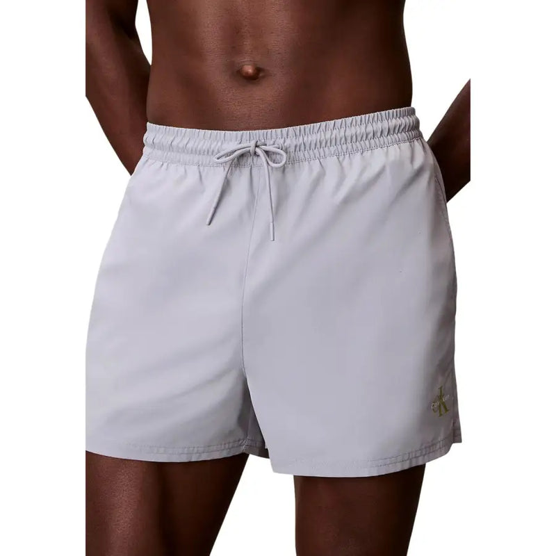Light gray Calvin Klein Jeans men swimwear swim trunks with drawstring waistband and subtle gold logo on lower right leg