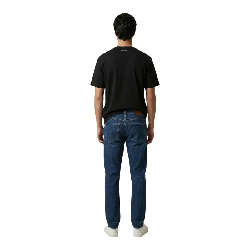 Dark blue denim jeans with classic five-pocket design and brown leather patch at waistband paired with calvin klein black cotton t shirt