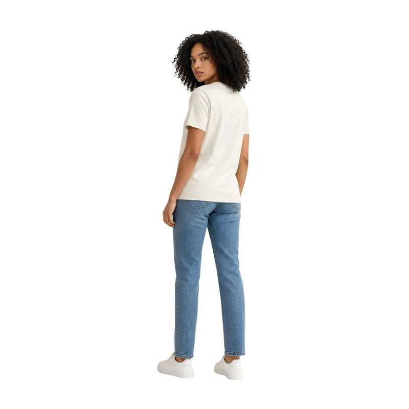 Eine Frau trägt ein weißes, kurzärmeliges Baumwoll-T-Shirt von Calvin Klein Jeans mit Rundhalsausschnitt und hellblaue Jeans.