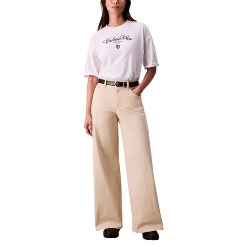Beigefarbene, weit geschnittene Jeans aus klassischem Denim in lockerer Passform, kombiniert mit einem weißen, kurzen Calvin Klein Jeans-T-Shirt mit Rundhalsausschnitt für Damen.