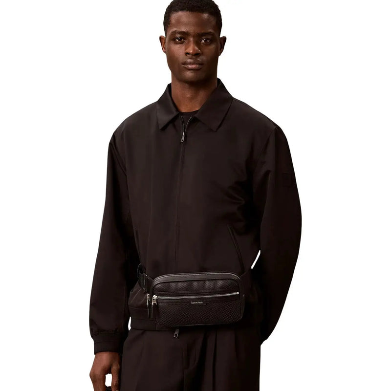 Schwarzes, strukturiertes Leder Calvin Klein Perforierte Herren-Bauchtasche aus Polyurethan mit silbernen Reißverschlüssen und dezentem Logo-Detail.