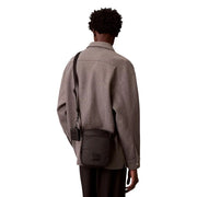 Schwarze Calvin Klein Herren-Puffertasche im Reporterstil mit Steppstruktur und rechteckigem Logo-Patch.