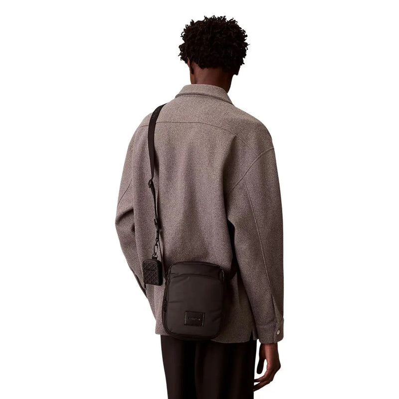 Schwarze Calvin Klein Herren-Puffertasche im Reporterstil mit Steppstruktur und rechteckigem Logo-Patch.