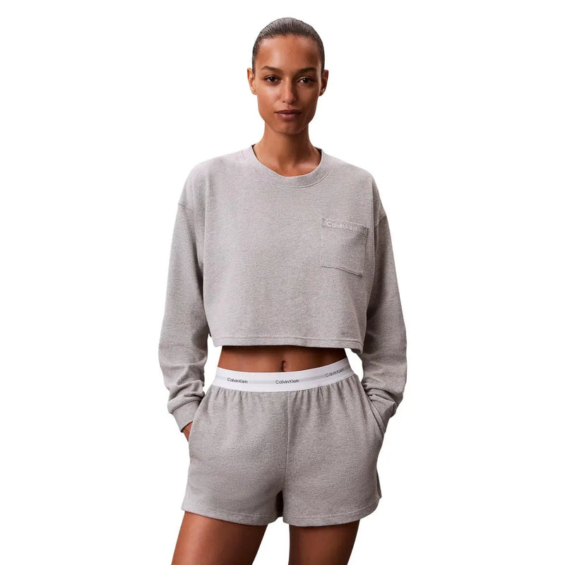 Graues, kurzes Sweatshirt mit kleiner Brusttasche und Calvin Klein Logo, kombiniert mit schwarzen Jersey-Baumwollshorts.