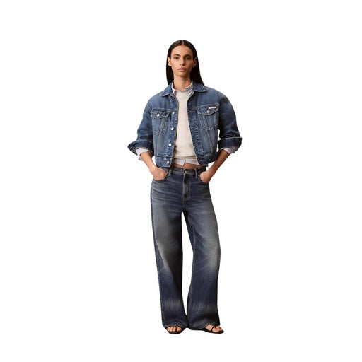 Eine Frau, die eine dunkelblaue Jeansjacke mit hochgekrempelten Ärmeln und eine weite Jeans mit einem weißen Baumwoll-Sweatshirt von Calvin Klein trägt.