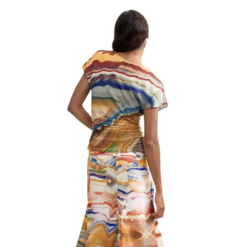 A woman wears a vibrant one-shoulder top and skirt with bold stripes in earthy tones featuring Desigual beige polyester t shirt