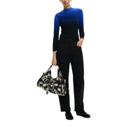 Schwarze Viskosehose für Damen von Desigual mit Taschen, kombiniert mit einer schwarz-weiß gemusterten Schultertasche mit überlappenden Gürtelschnallen.