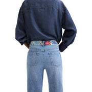 Desigual Damen-Jeans aus blauem Baumwoll-Denim, getragen mit einem farbenfroh gemusterten Gürtel mit einer bunten, gestickten Rosenschnalle