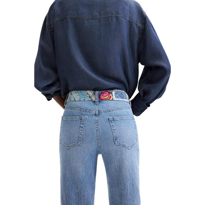 Desigual Damen-Jeans aus blauem Baumwoll-Denim, getragen mit einem farbenfroh gemusterten Gürtel mit einer bunten, gestickten Rosenschnalle
