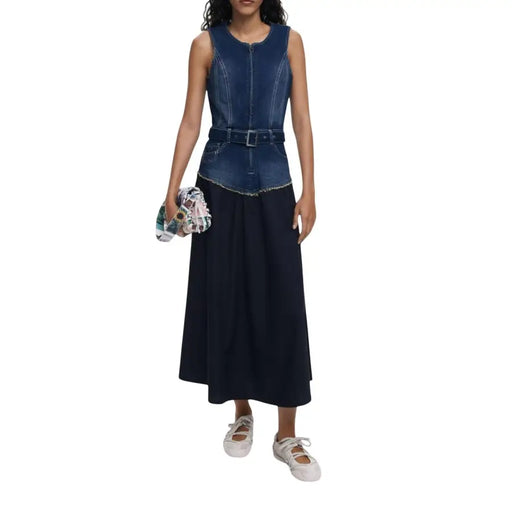 Women wearing a two-tone denim and black maxi dress with belt and multicolored clutch