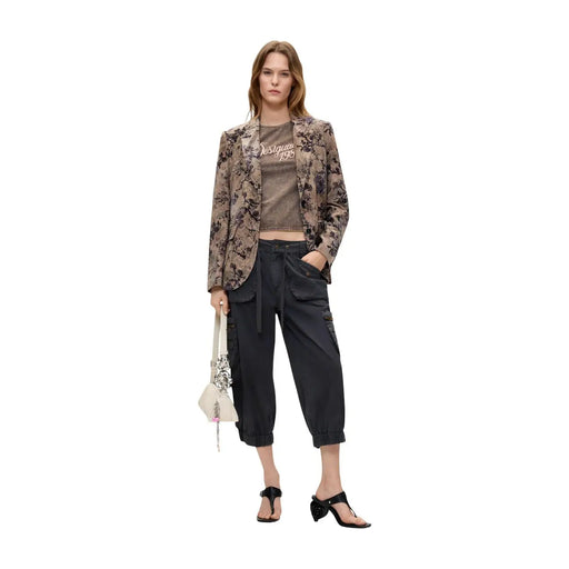 Eine Frau trägt einen beigefarbenen Polyesterblazer von Desigual mit braunem Blumenmuster über einem passenden kurzen T-Shirt.