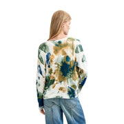 Eine Frau trägt eine weiße Viskosebluse von Desigual mit langen Ärmeln und einem abstrakten blau-grünen Strickmuster.