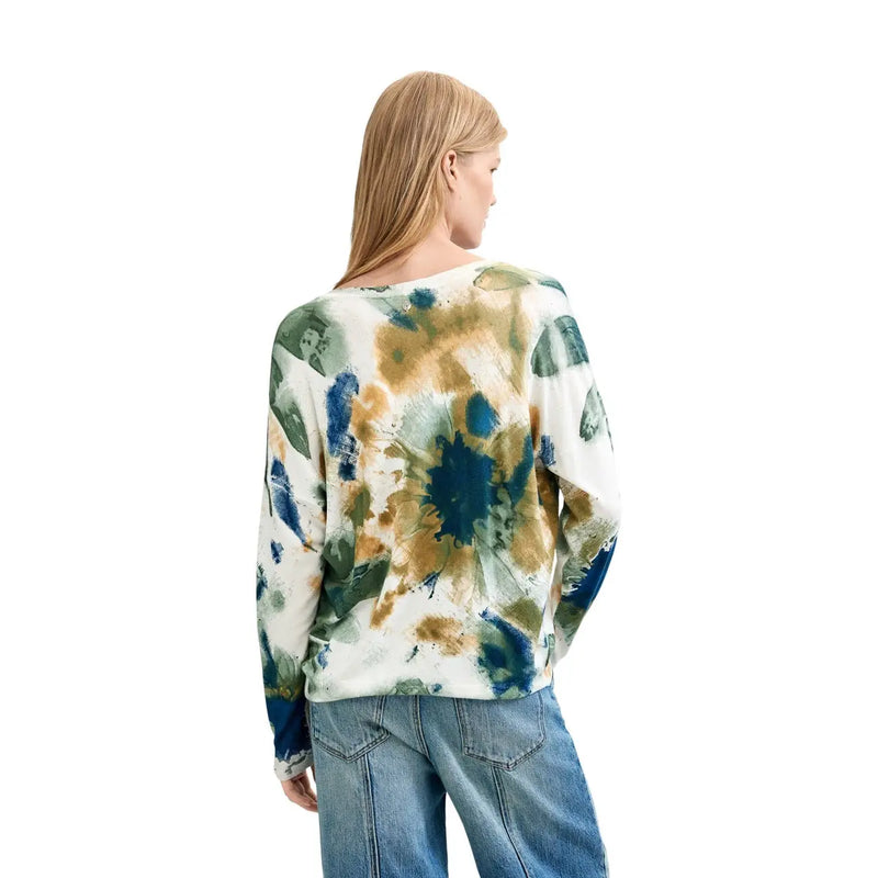 Eine Frau trägt eine weiße Viskosebluse von Desigual mit langen Ärmeln und einem abstrakten blau-grünen Strickmuster.