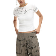 Weißes Kurzarmhemd top mit schwarzem, handgeschriebenem Text, kombiniert mit einer grauen Desigual Damenhose aus Viskosemischgewebe mit Reißverschluss und Muster.