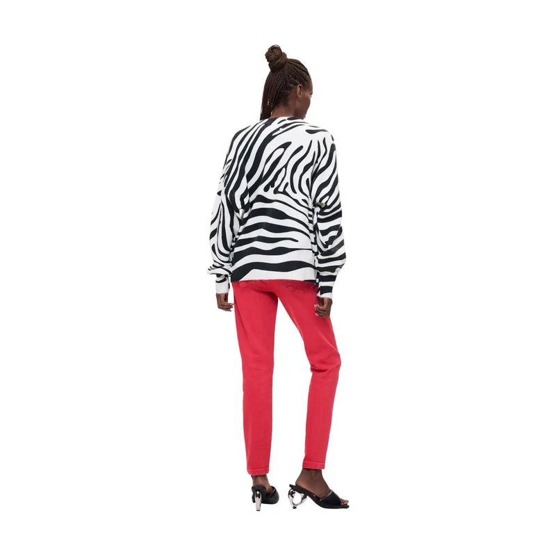 Eine Frau trägt einen weißen, langärmeligen Desigual-Strickpullover aus Acrylmischgewebe mit Zebrastreifen in regulärer Passform und roter Hose.