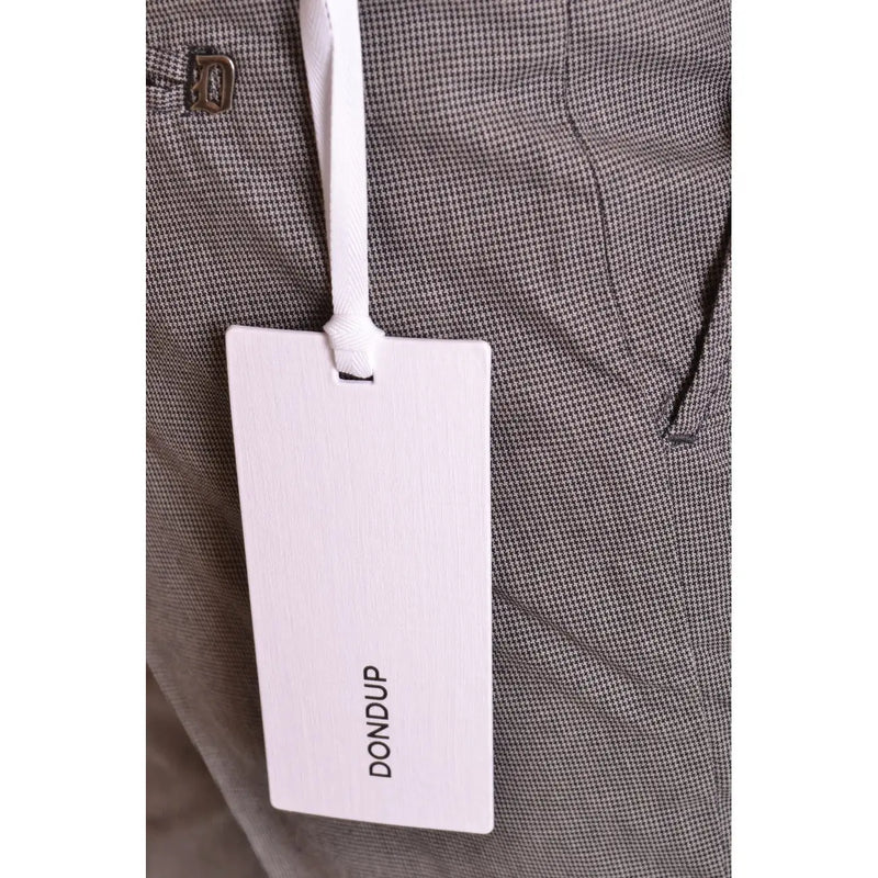 White rectangular brand tag with dondup printed in black attached by white ribbon to grey houndstooth fabric of men’s cotton trousers