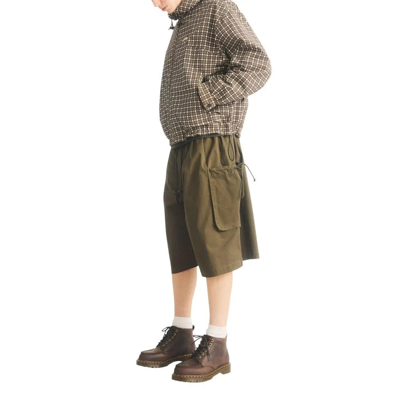 Olivgrüne Cargoshorts mit Kordelzug im Bund und Taschen, abgebildet neben braunen Dr. Martens Herren-Chukka-Boots aus Leder (Modell Lowell).