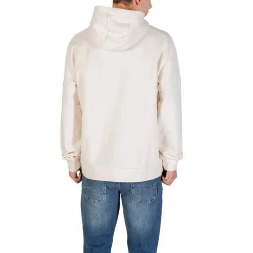 Men’s cream-colored hooded sweatshirt with front pockets paired with blue jeans