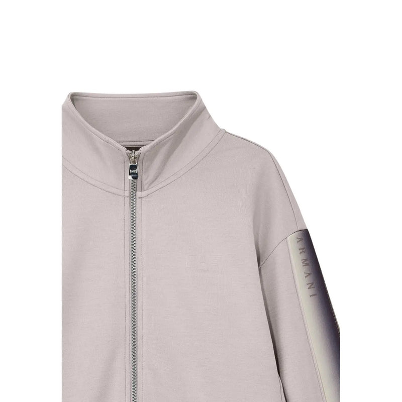 Eine elegante, hellgraue Armani-Jacke mit Reißverschluss, farbverlaufendem Ärmeleinsatz und Metallreißverschluss, die perfekt zum beigefarbenen EA7-Jumpsuit aus Baumwollmischgewebe für Damen passt.