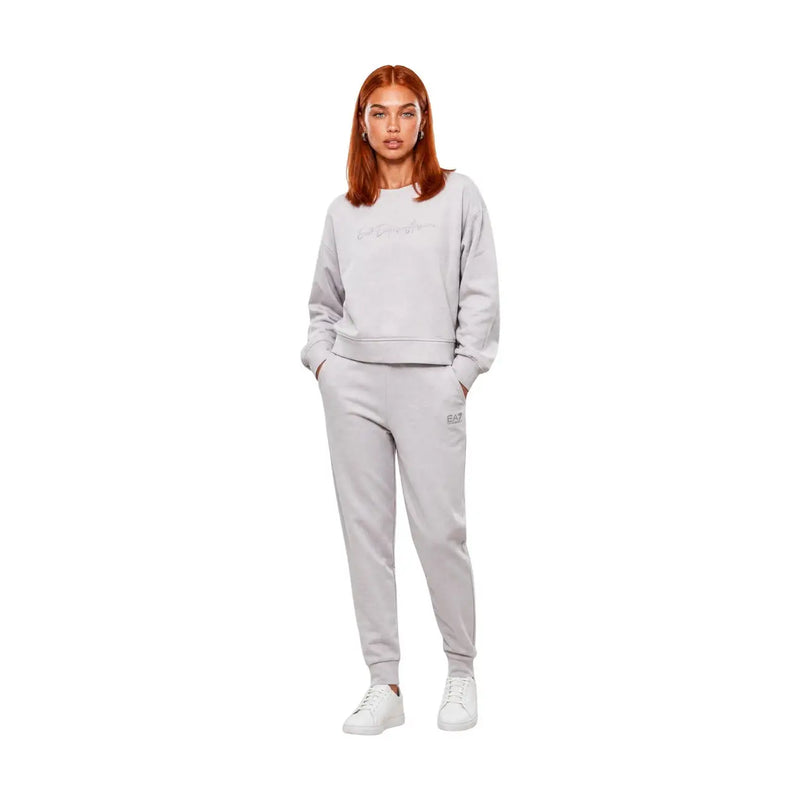 Eine Frau trägt einen grauen Baumwoll-Jumpsuit von ea7 mit Rundhalsausschnitt, ein hellgraues Sweatshirt und eine passende Jogginghose.