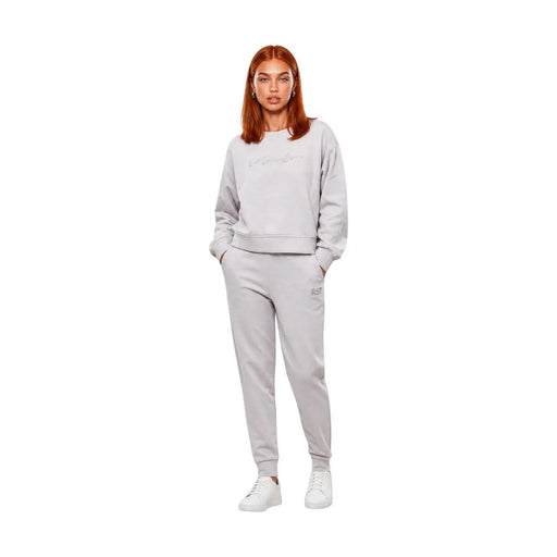Eine Frau trägt einen grauen Baumwoll-Jumpsuit von ea7 mit Rundhalsausschnitt, ein hellgraues Sweatshirt und eine passende Jogginghose.