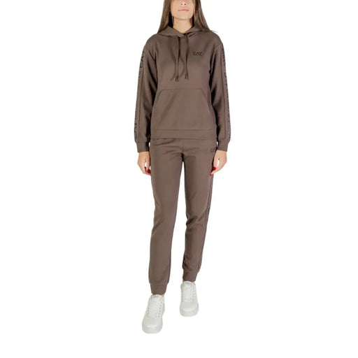 Women wearing a brown hooded tracksuit with white sneakers in EA7 printed black jumpsuit display