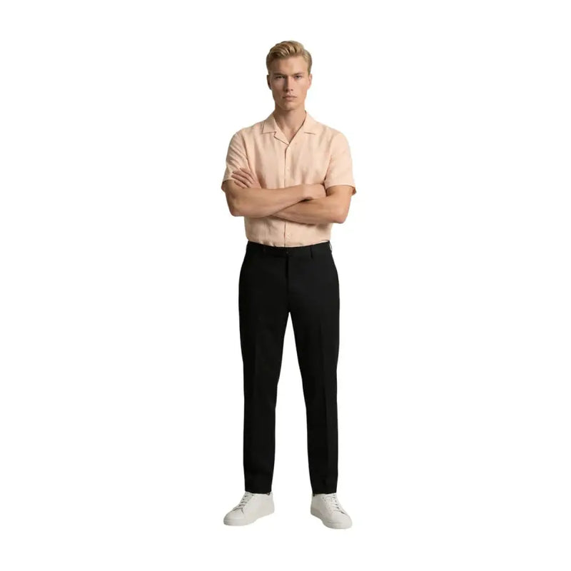 Ein Mann, der gianni lupo Schwarze Herrenhose aus Polyester-Viskose, kombiniert mit einem hellpfirsichfarbenen Kurzarmhemd und weißen Sneakers.